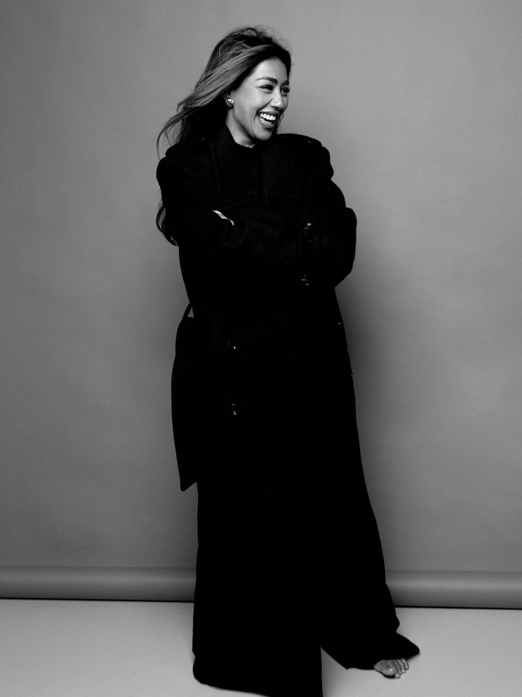 Aarti laughing in a long black coat, arms crossed