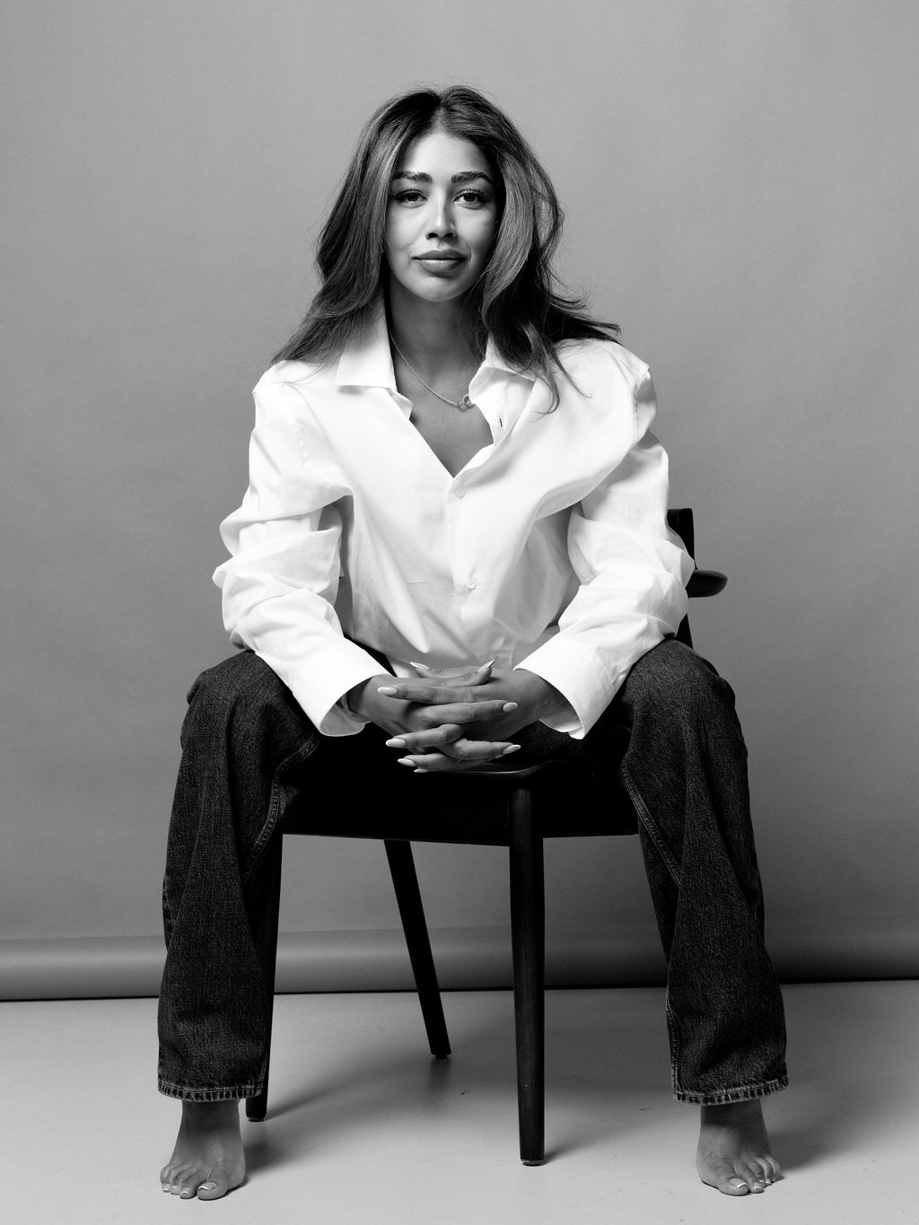 Aarti seated on a stool in a white shirt, looking at the camera